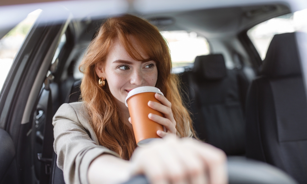 A happy woman drives while drinking from an orange coffee cup